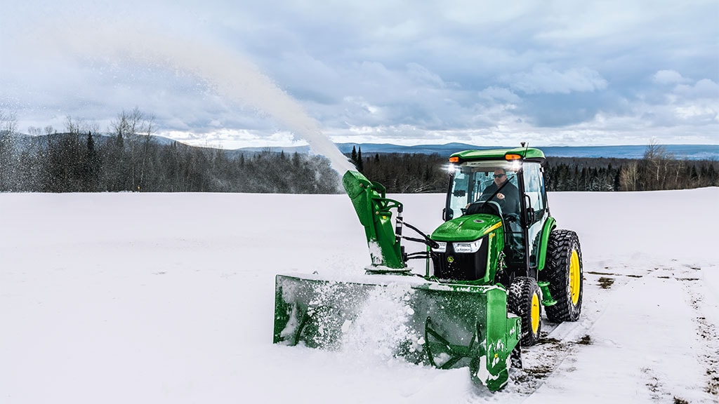Person using a 4075R Compact Tractor equipped with a snow blower to clear snow.