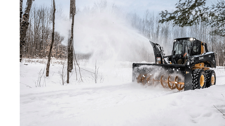 Person using a skidsteer equipped with a snow blower to clear snow