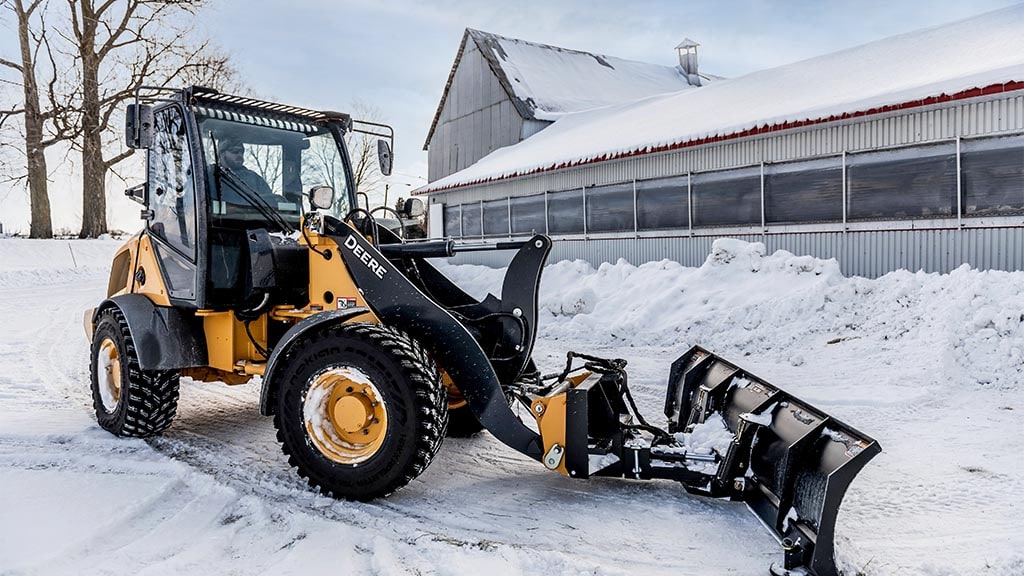 Person clearing snow from parking lot using a compact wheel loader