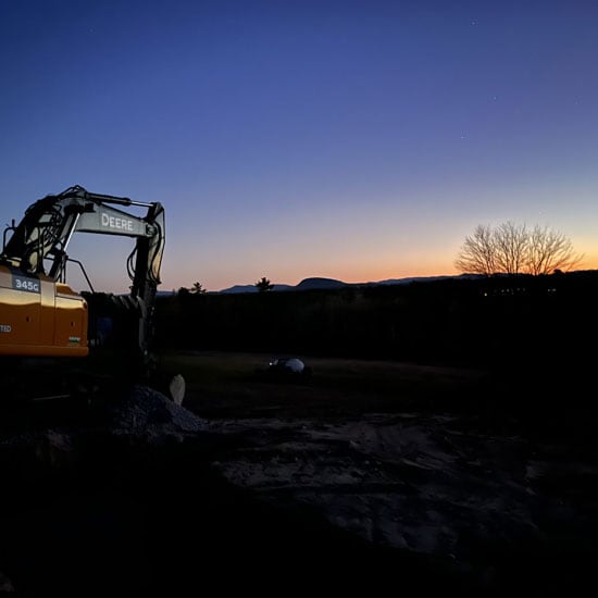 John Deere 345G Excavator parked as the sun sets in the distance.