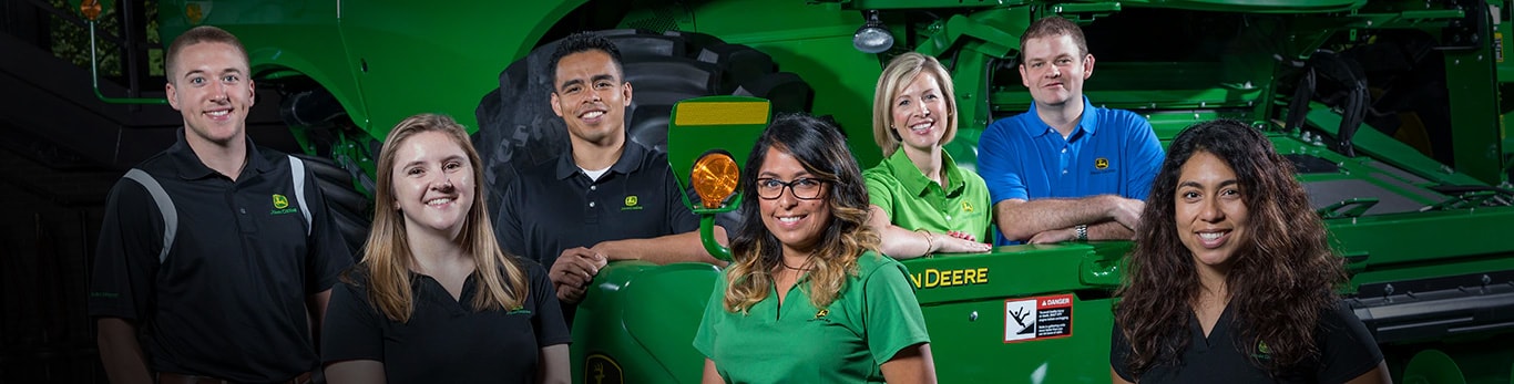 Group of employees from all walks of life posing in front of a John Deere tractor