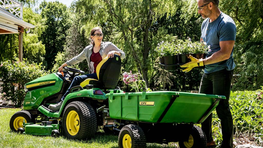 woman getting onto a mower while a man puts flowers in the mower cart