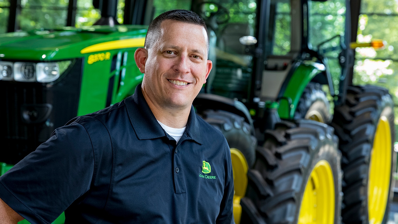 Military veteran standing proudly in front of a John Deere tractor