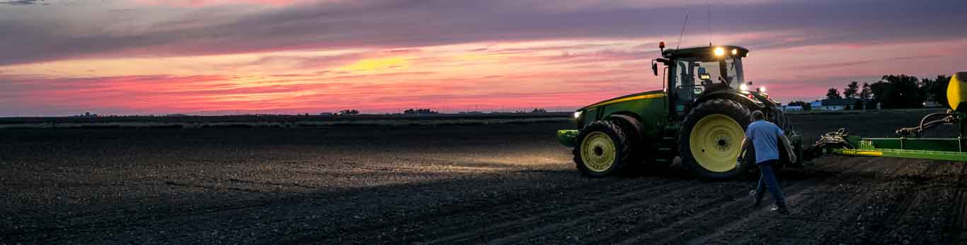 Man walking in a field next to a John Deere tractor during sunset