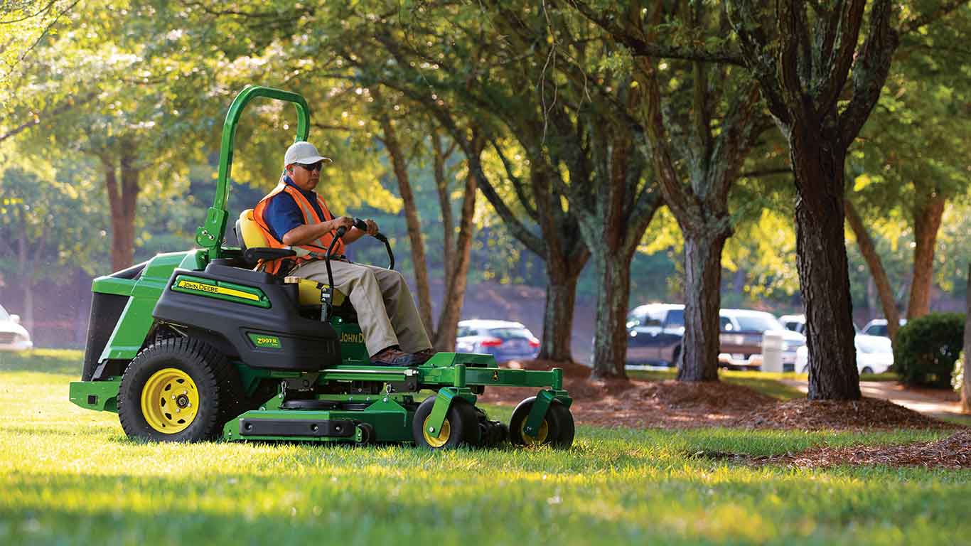 Man with an orange vest and white hat landscaping with a John Deere Zero Turn mower