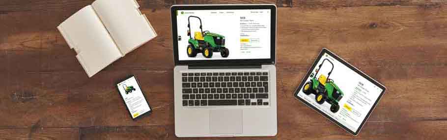 A computer, tablet, and mobile phone on a wooden table with the John Deere 1023E Compact Tractor on the screens