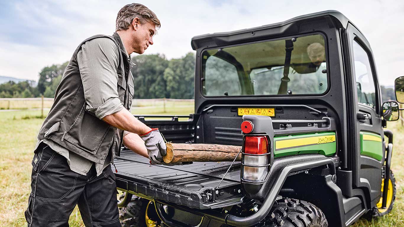 Man in a field loading wood into the bed of a John Deere Gator Utility Vehicle