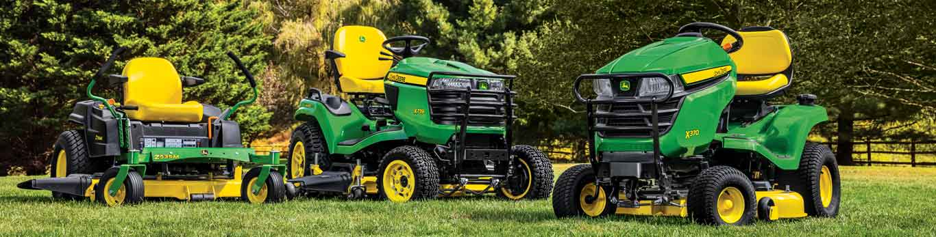 John Deere Lawn Tractors and a Zero-Turn ZTrak Mower sitting in a line-up with trees in the background
