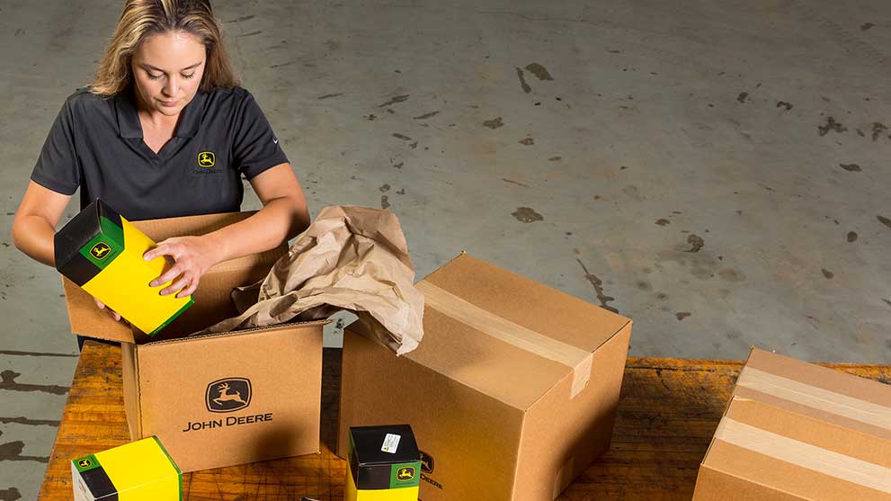 A person packages John Deere parts up into shipping boxes