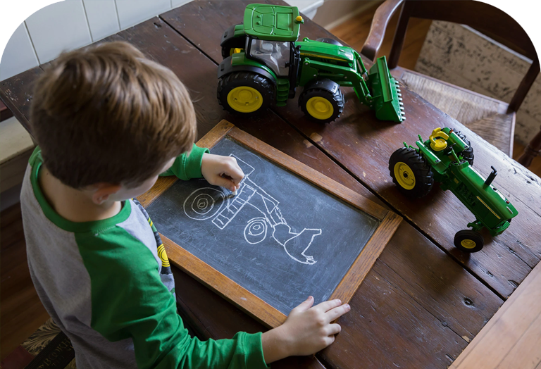 A boy draws a tractor on a chalkboard