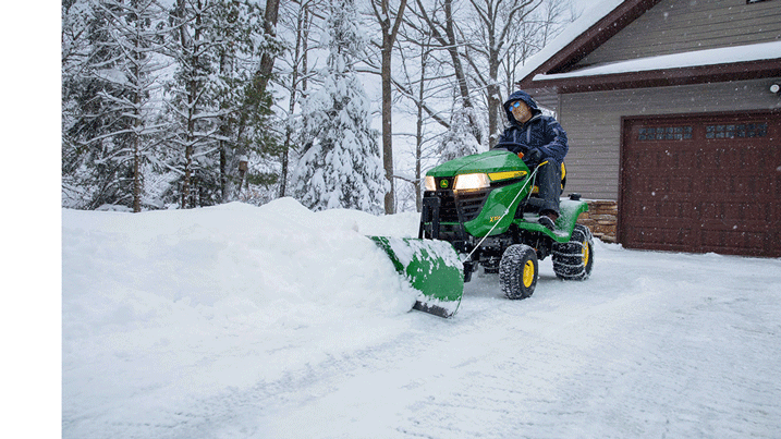 Person clearing driveway of snow using a lawn tractor equipped with a blade