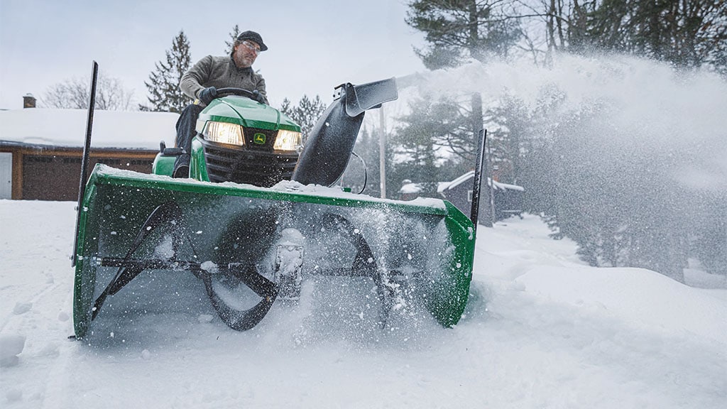 Person using a lawn tractor equipped with a snot blower to clear snow from driveway.