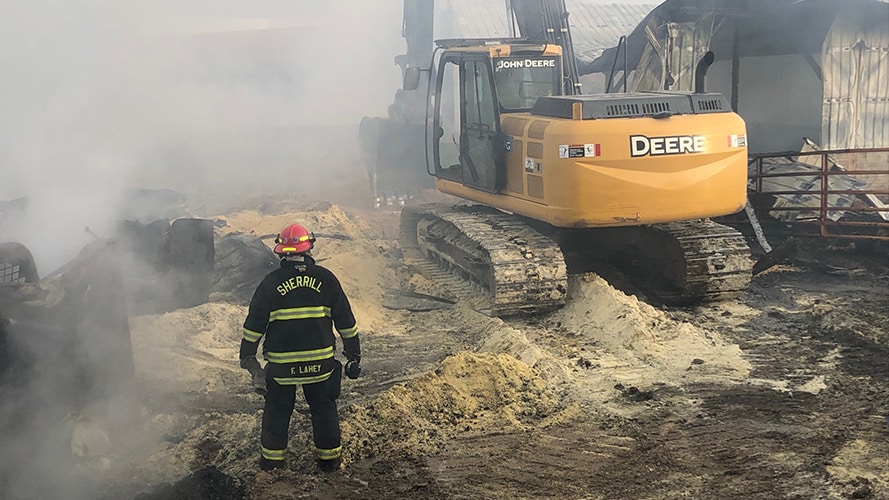 A volunteer firefighter walks near John Deere equipment in the aftermath of a fire
