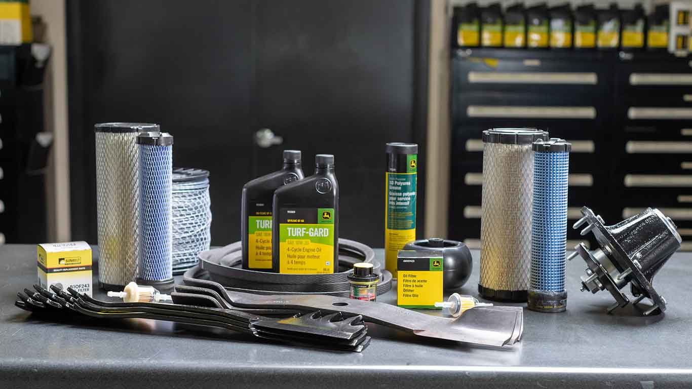 Spread of John Deere parts on a tool bench including blades, filters, and replacement parts