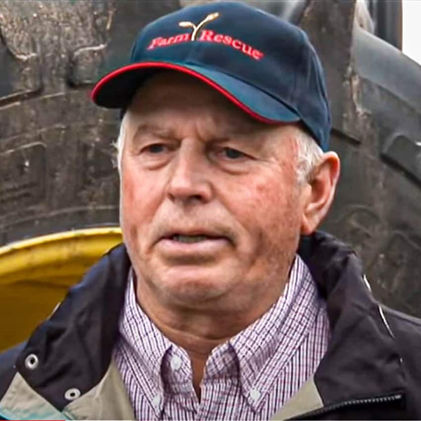 Ron Behm standing in front of a John Deere tractor with Farm Rescue hat and coat on