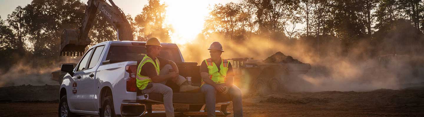 Two people sit on the tailgate of a dealer service truck at sunrise