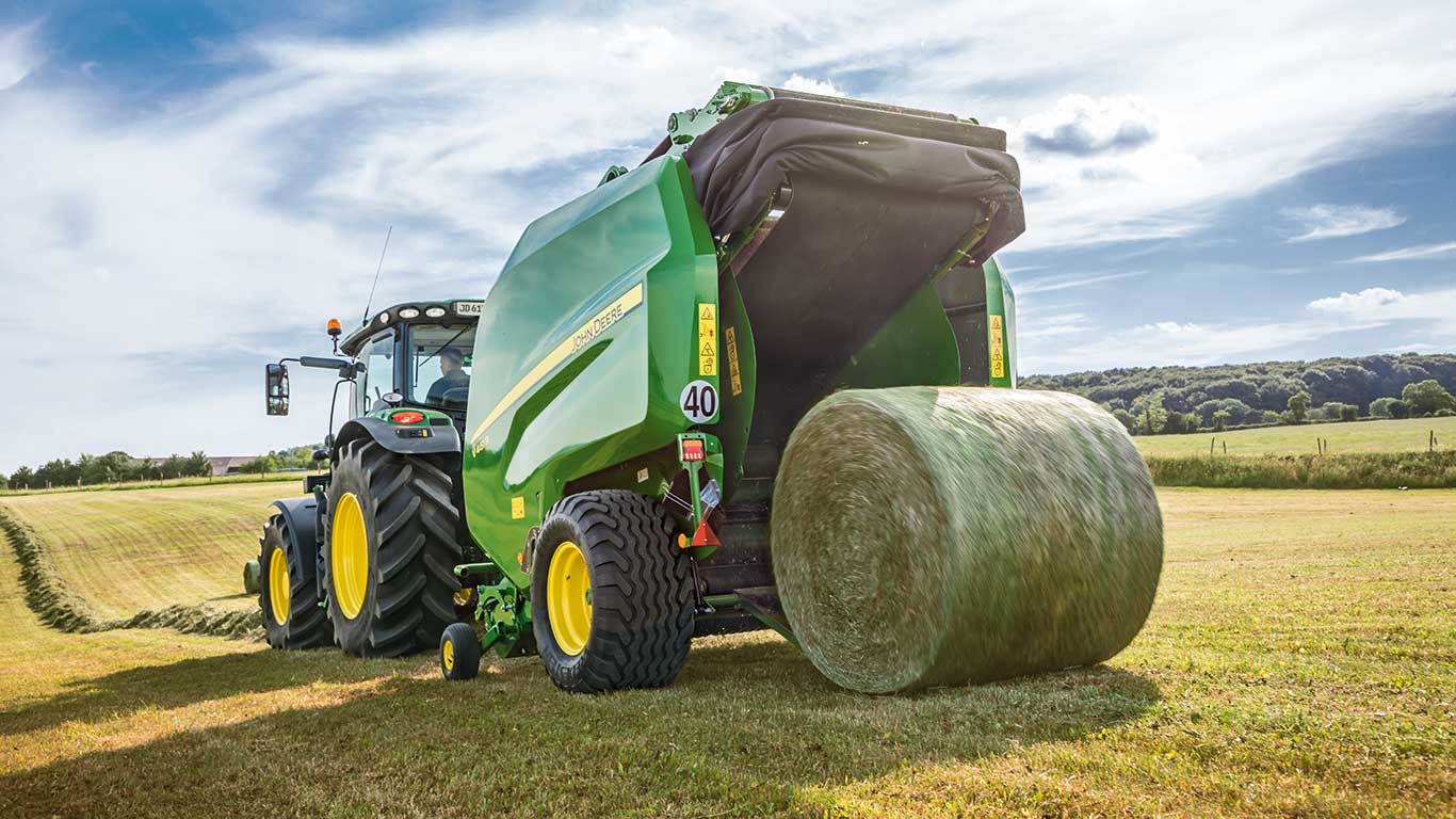 John Deere tractor with round baler drives through a field